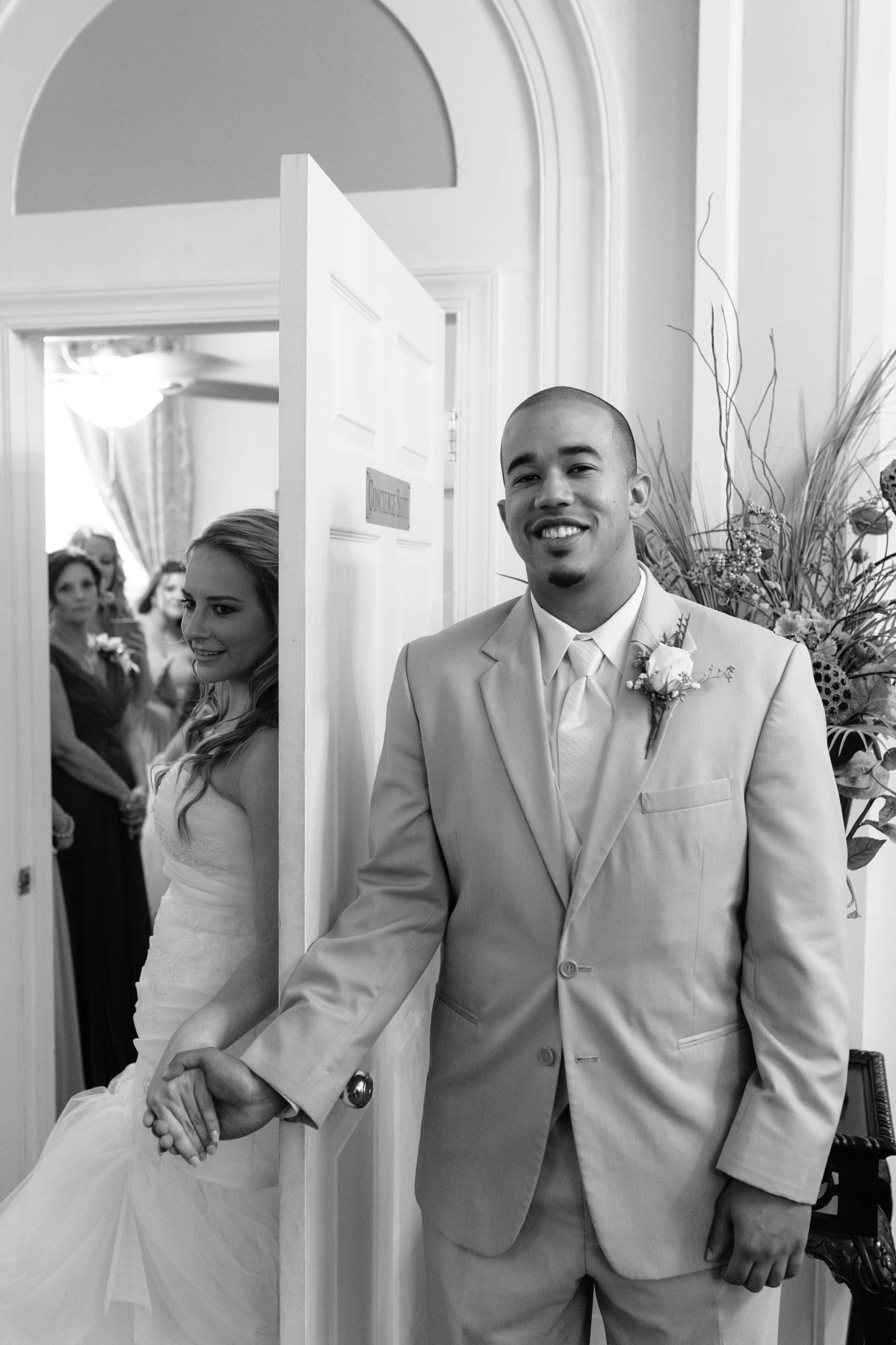 Bride and groom holding hands behind door without seeing each other