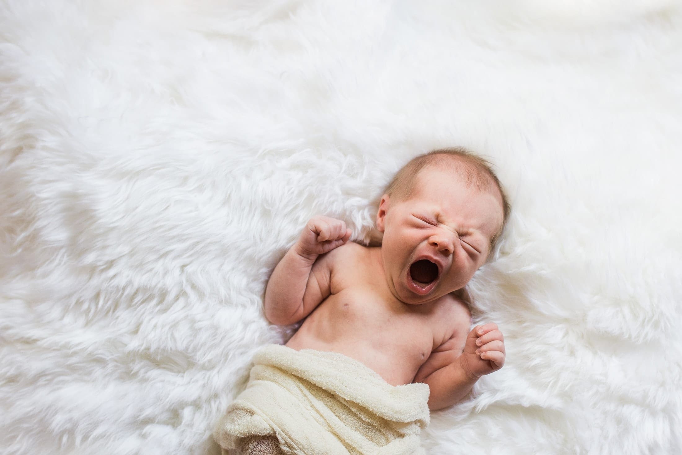 Baby yawns on white rug