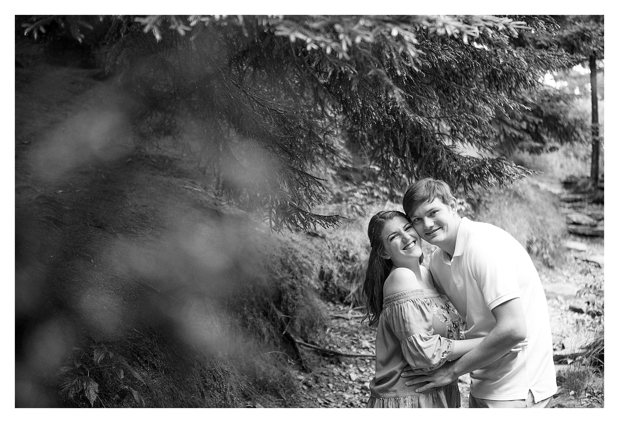 Black and white photo of young engaged couple hugging laughingly while smiling at camera