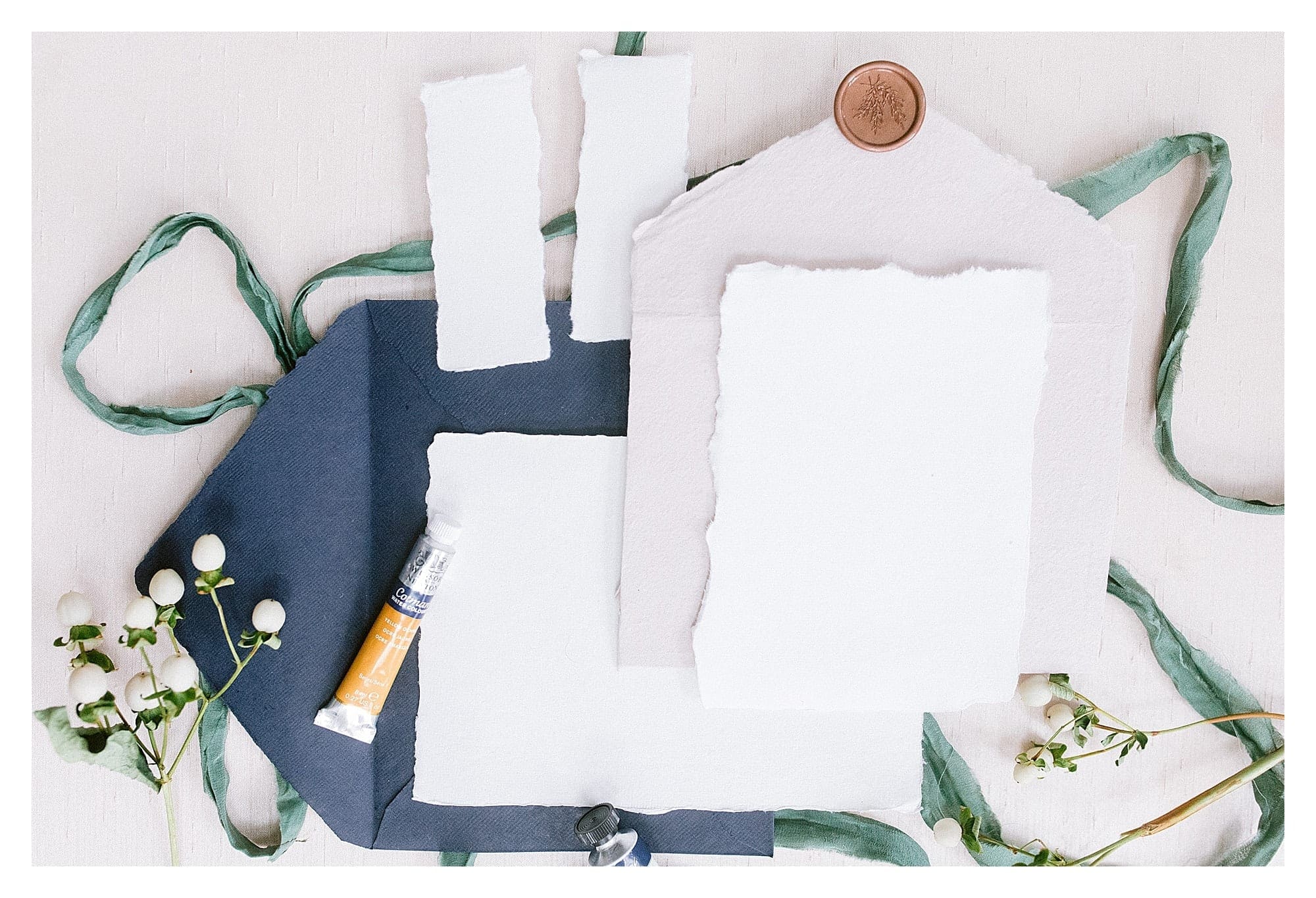 Calligraphy paper and envelope flatlay with green foliage and small silver paint tubes photography by Kathy Beaver