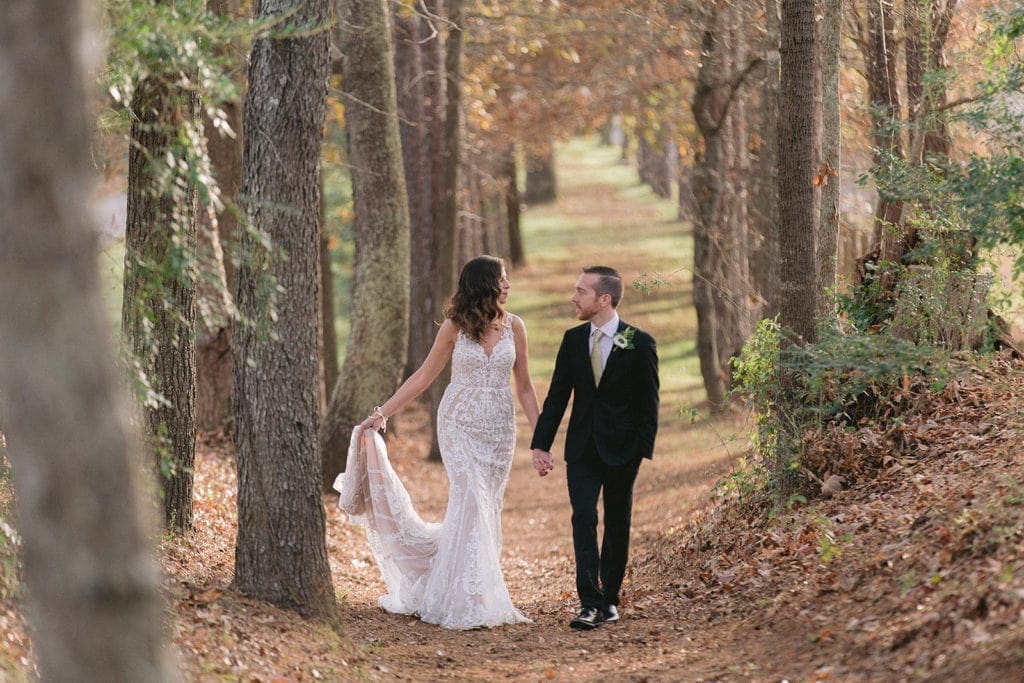 Fall wedding with bride and groom walking down path of trees.