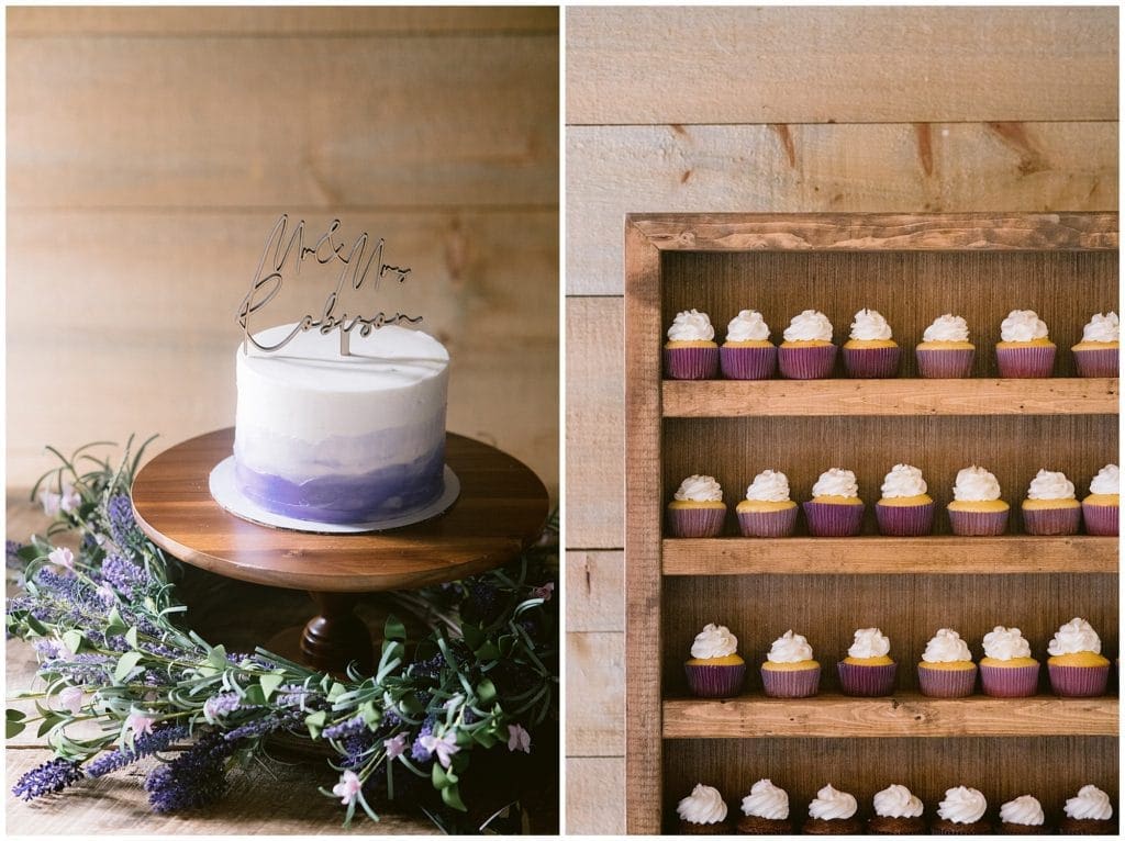 A purple and white wedding cake with a wooden cake topper that reads "Mr & Mrs Robinson", next to a wall of shelving full of purple cupcakes | Asheville Wedding Photographer