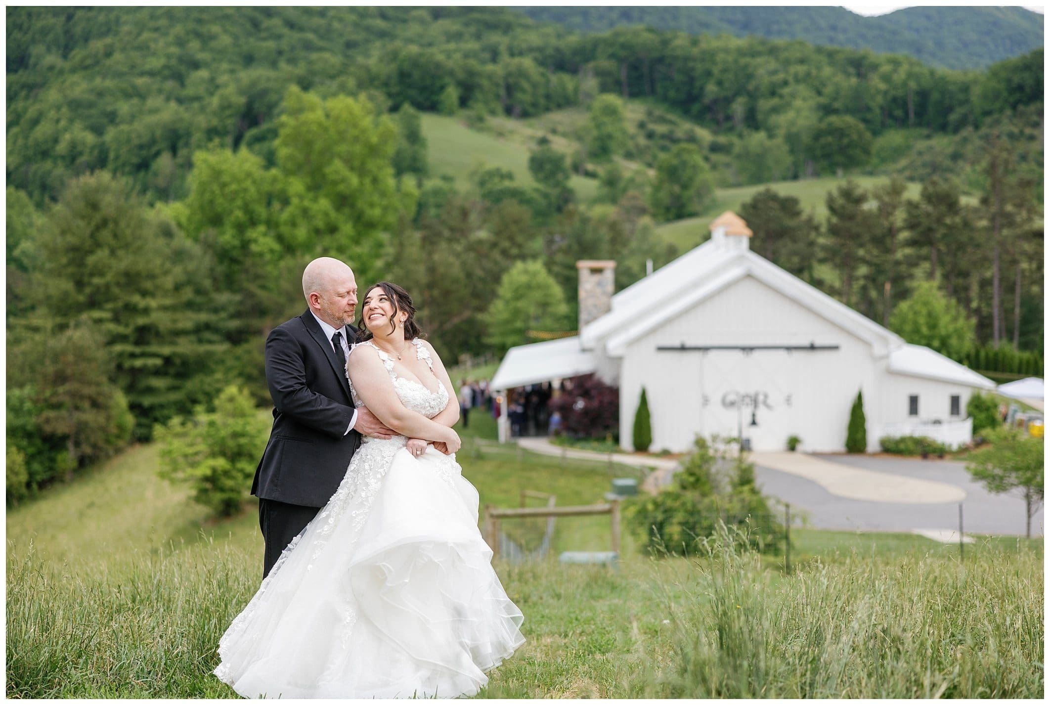 Bride and groom laughing in field with wedding venue behind them. 
