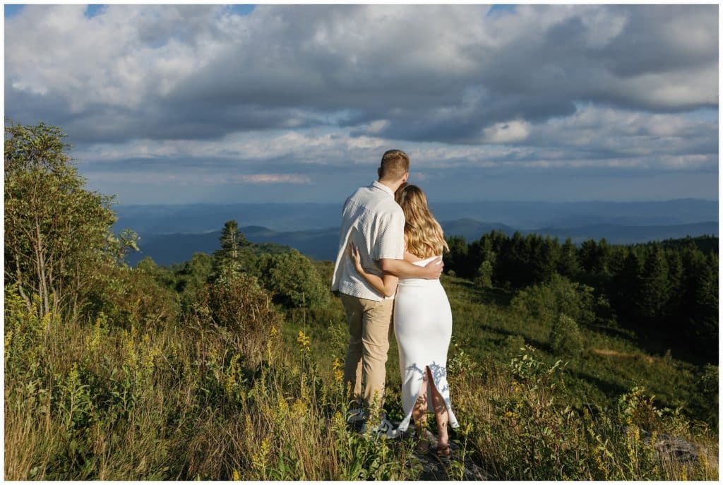 A couple is standing on top of a hill overlooking the mountains at an Engagement session at Black Balsam & Graveyard Fields