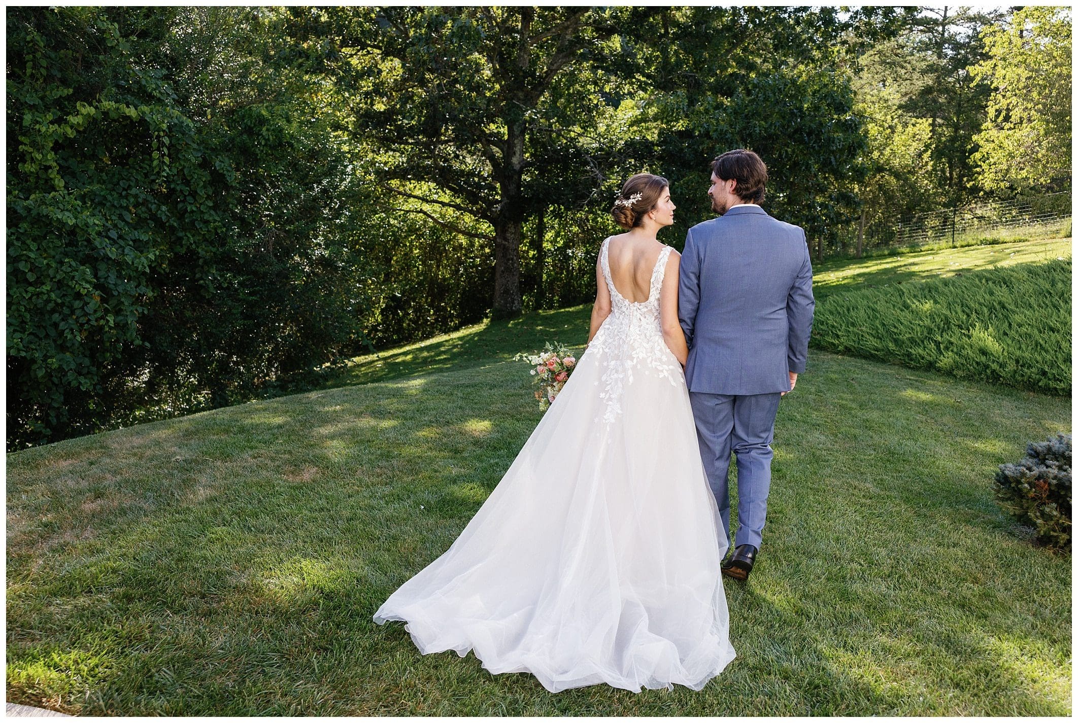 A bride and groom walking through a grassy field.