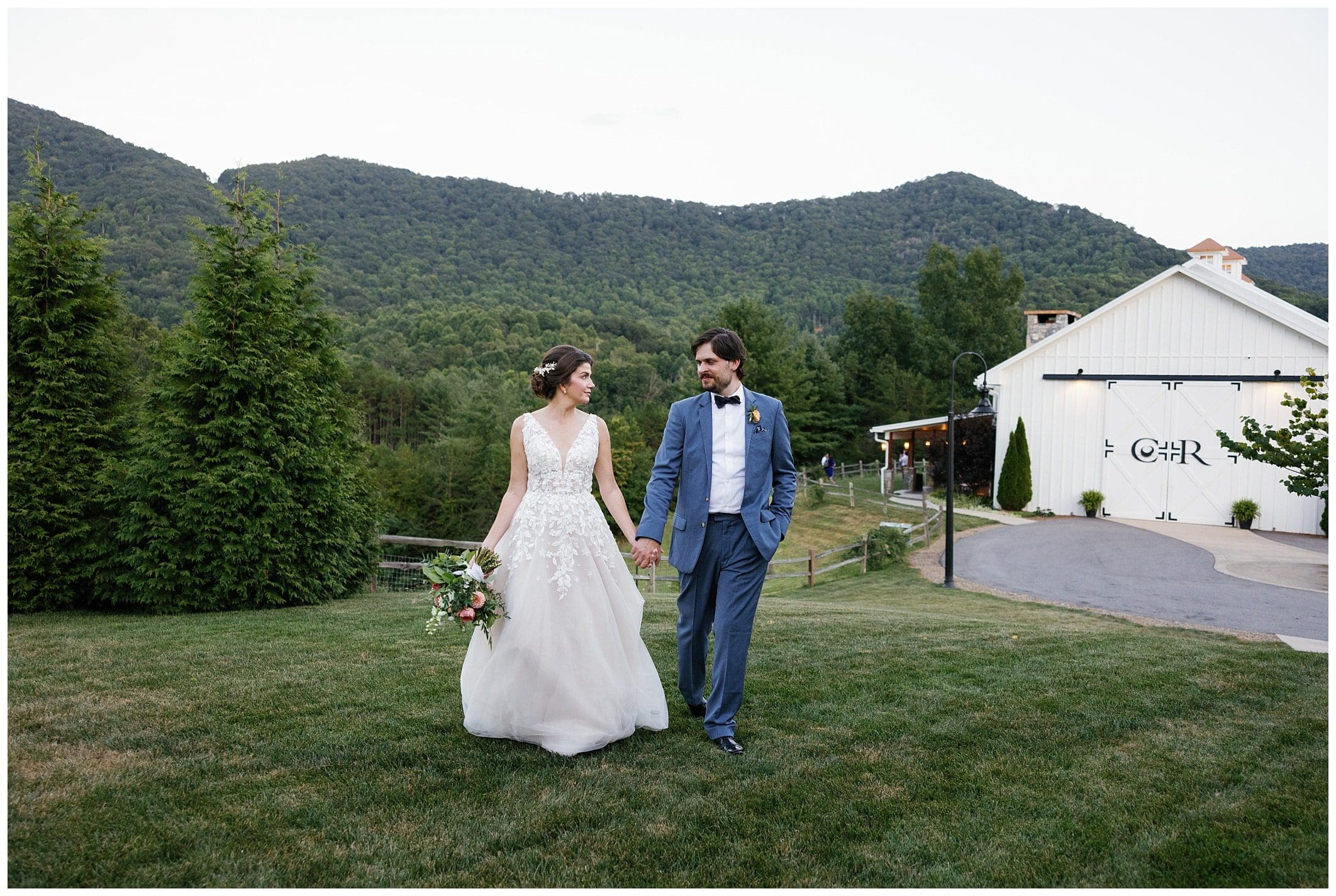 A bride and groom holding hands in front of mountains.