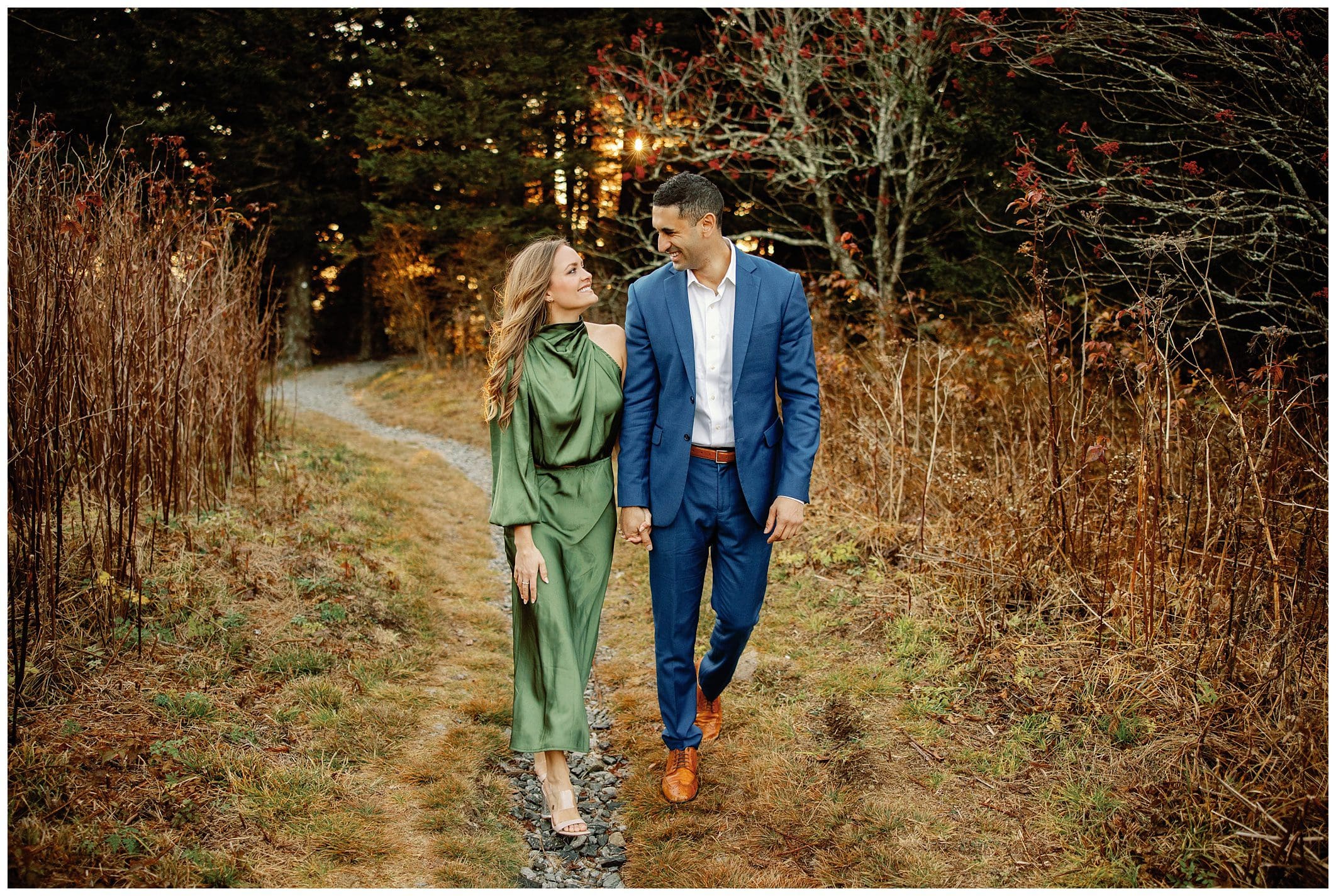 A couple enjoying their sunrise engagement walk together on a path surrounded by autumn foliage.