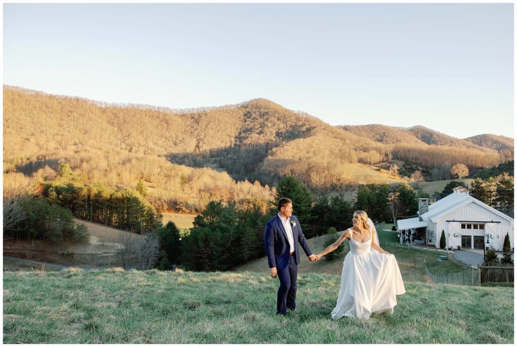 A bride and groom walking in a field with mountains in the background.