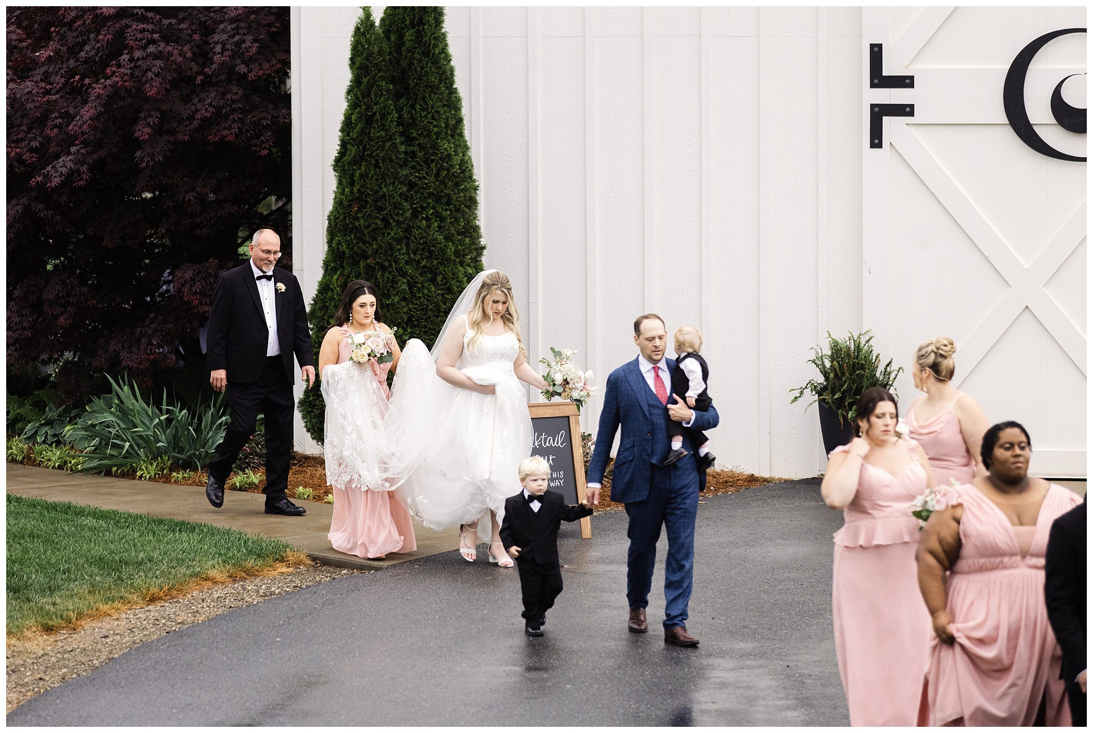 Wedding procession outdoors with a bride and groom followed by guests and a man carrying a child at Chestnut Ridge.