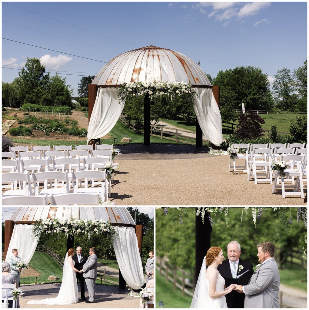 A couple stands under a flower-decorated pavilion during an outdoor wedding ceremony, with an officiant and rows of white chairs on either side.