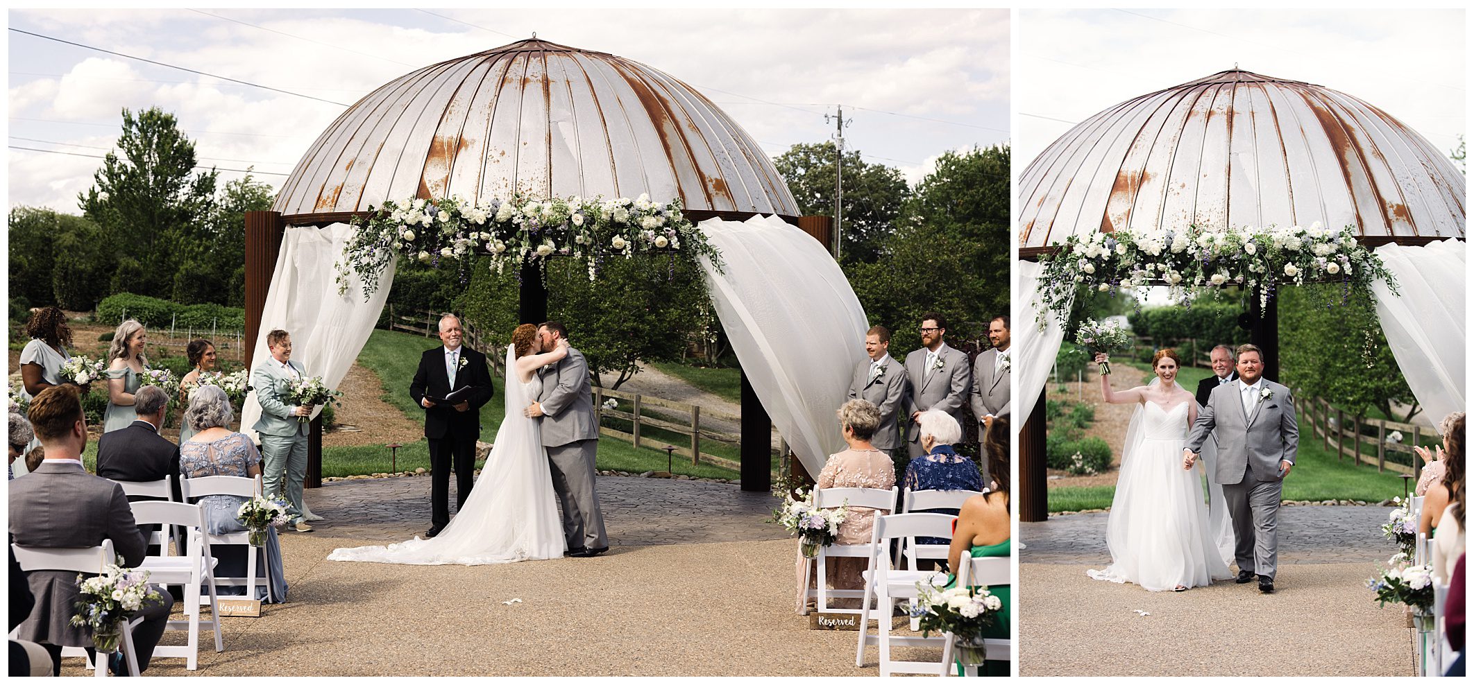 A couple kisses under a floral-decorated, rusted dome structure during an outdoor wedding ceremony. The bride in a white gown and groom in a grey suit are in front of seated guests.