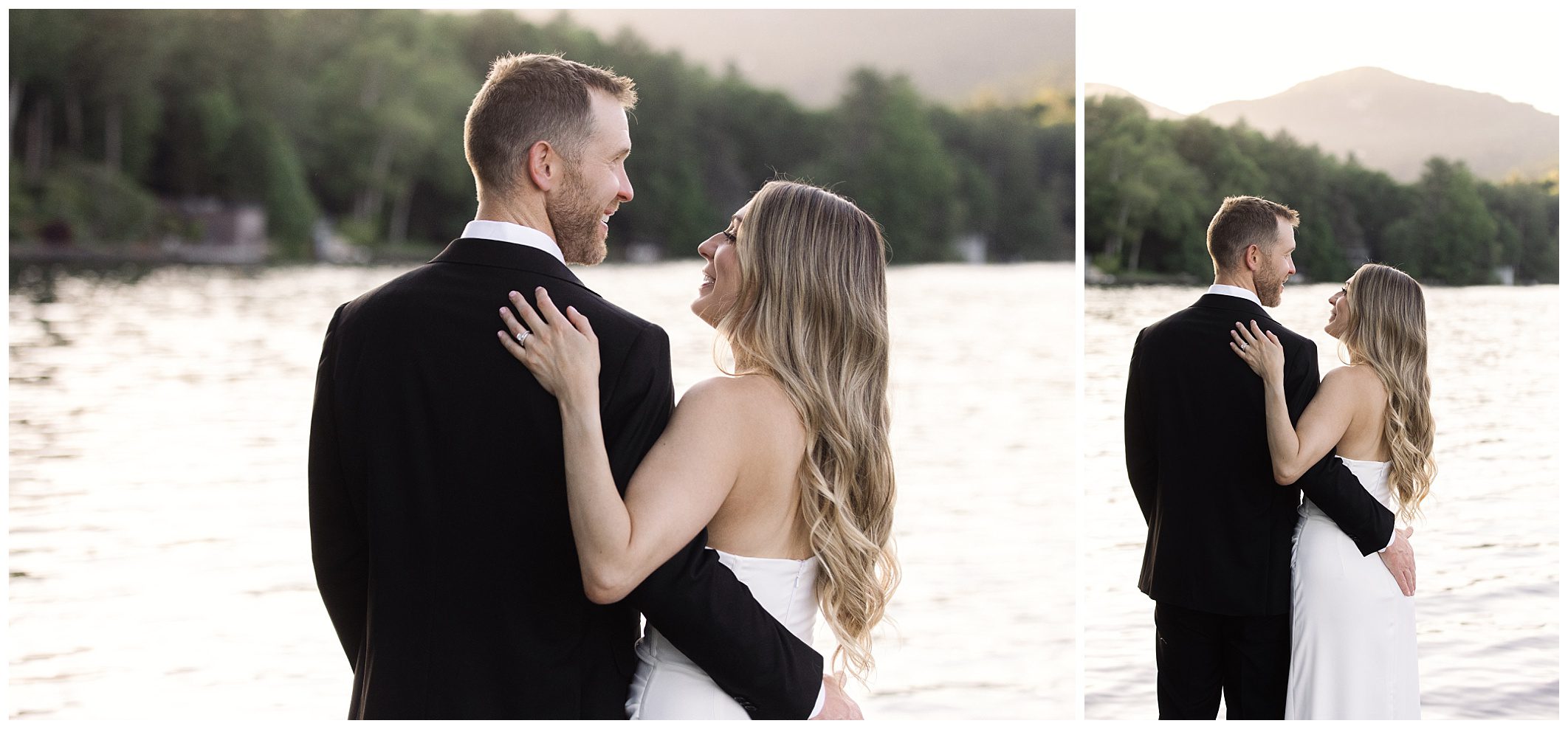 A couple dressed in formal attire stands by a lakeside, facing each other and smiling. The background features water and a tree-covered shoreline with hills in the distance.