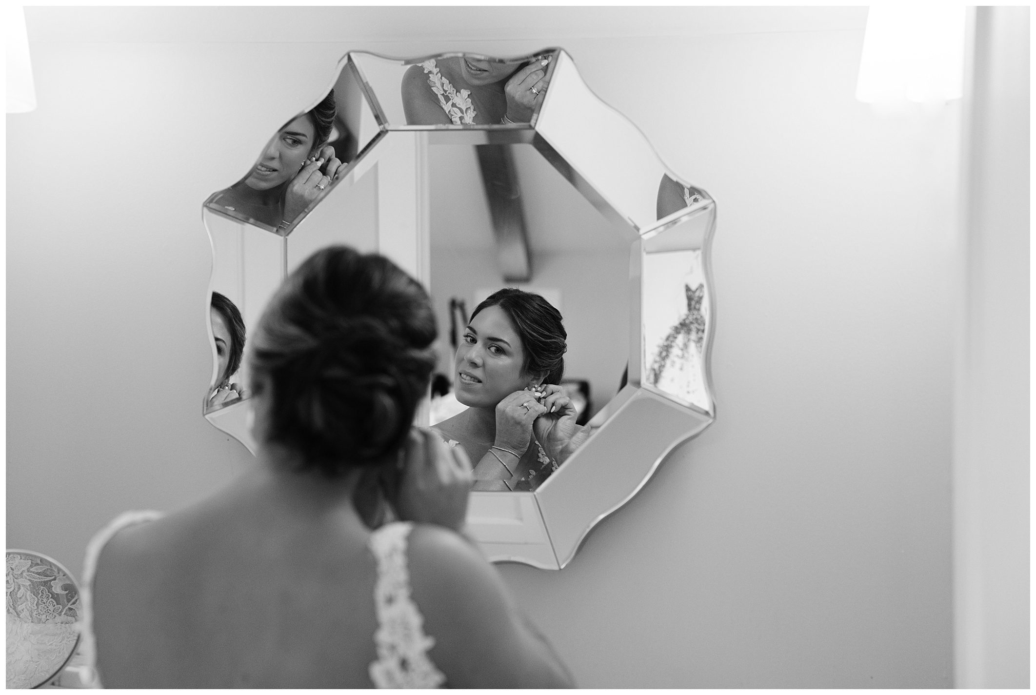 A woman adjusts her earring while looking into a multi-sided mirror in this black and white photograph.