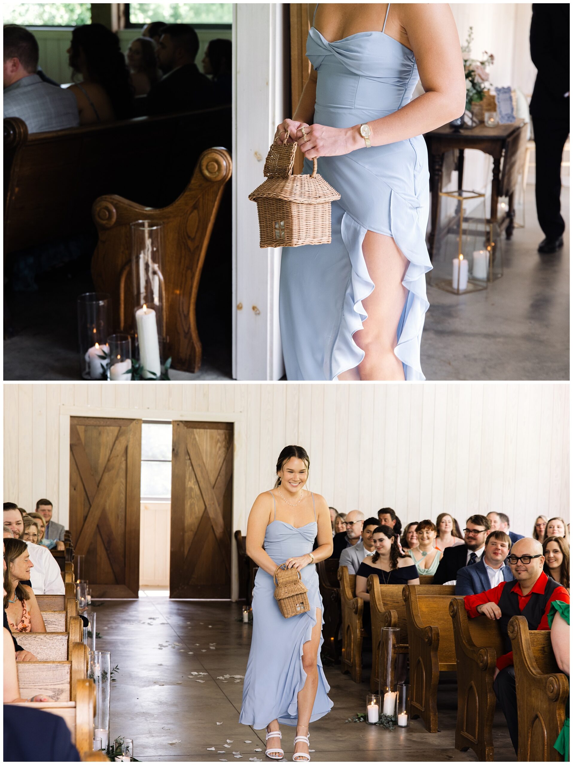 A woman in a light blue gown walks down an aisle inside a venue. She holds a small wicker basket and is watched by seated guests on wooden benches. Candles in tall glass holders decorate the aisle.