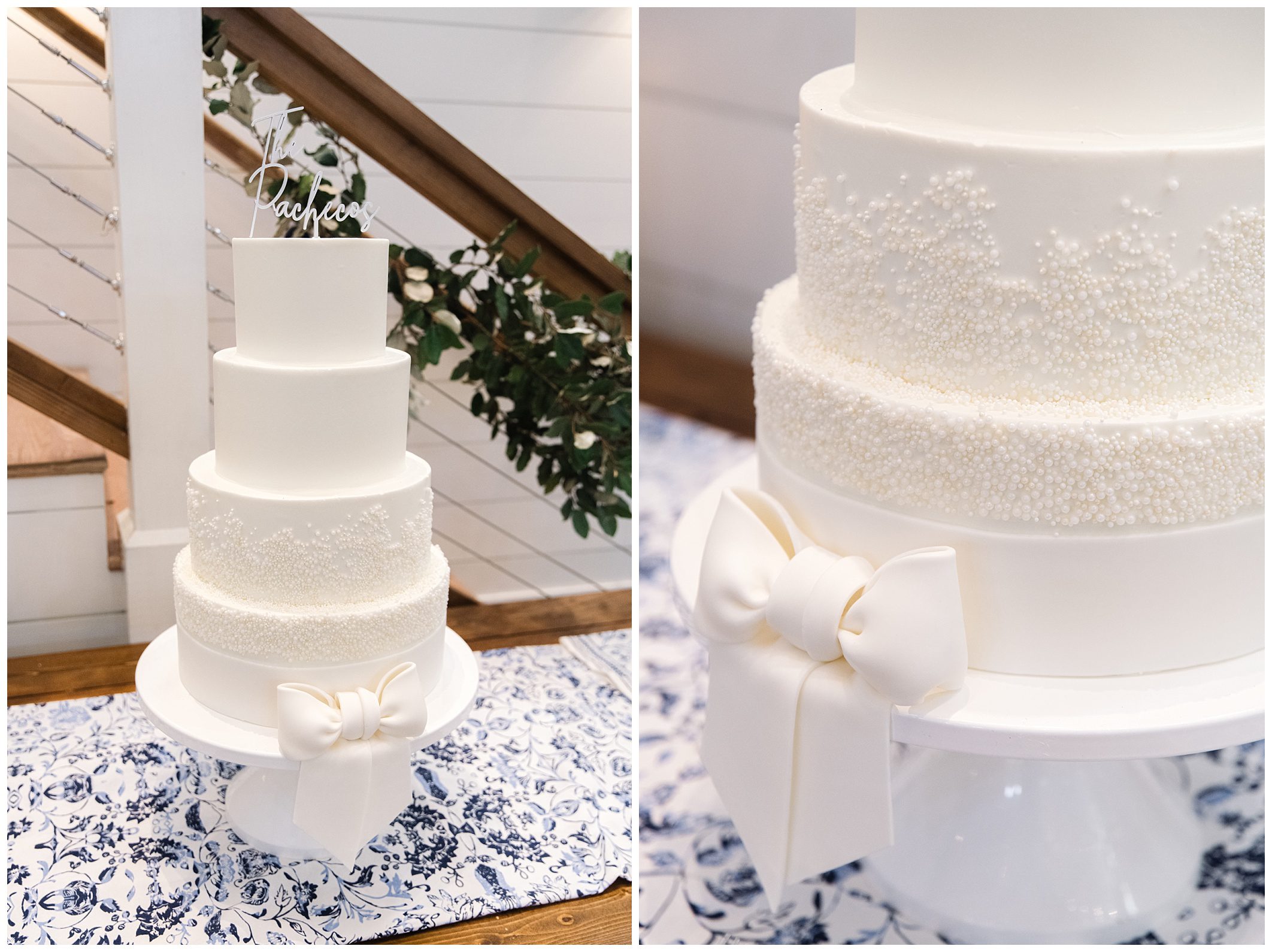 A four-tiered white wedding cake decorated with intricate, small pearl-like designs, a large white bow at the base, and a name topper. The cake is displayed on a table with a blue-patterned cloth.