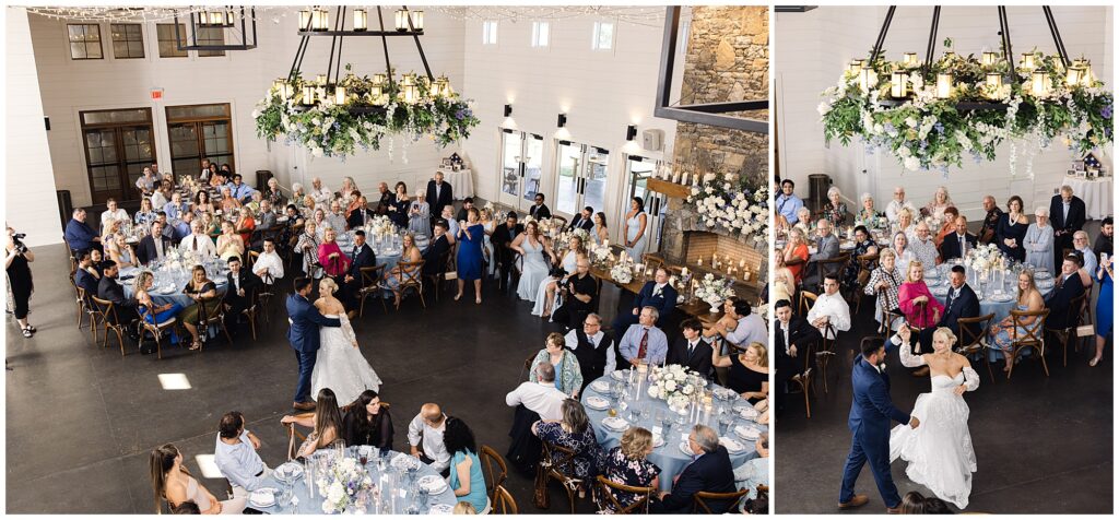 A bride and groom share their first dance in a large, decorated hall filled with seated guests watching from round tables. Chandeliers with greenery hang from the ceiling.