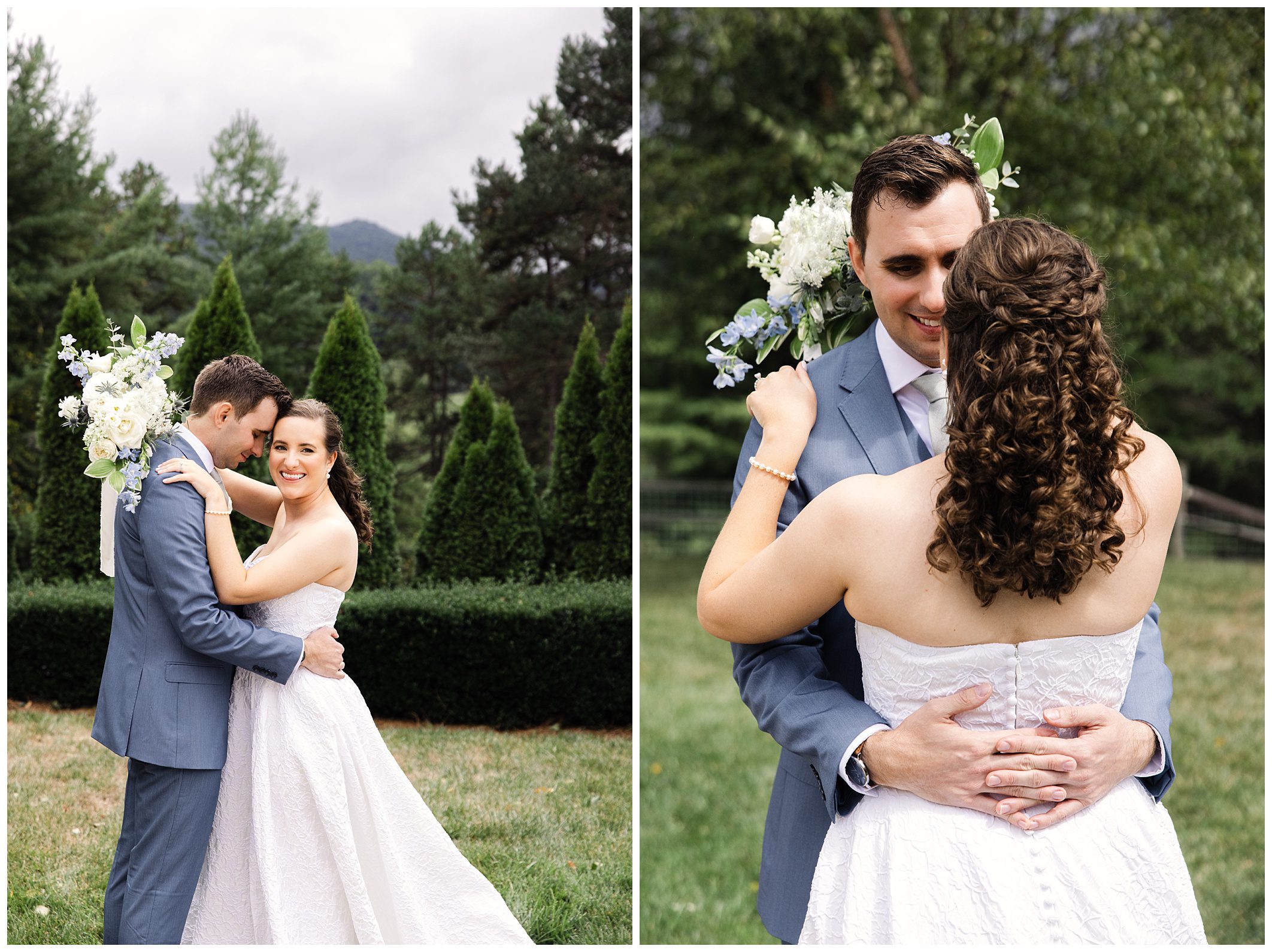 A couple, with the woman in a white dress and the man in a blue suit, embraces outdoors in a grassy area with trees and mountains in the background. The woman holds a bouquet of flowers.