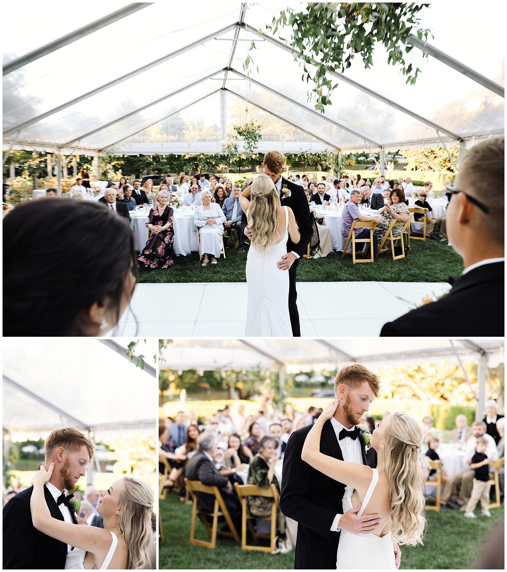 A newlywed couple dances under a clear tent with onlookers seated at tables. The groom wears a black suit and the bride a white dress. Bright outdoor setting with greenery and clear skies.