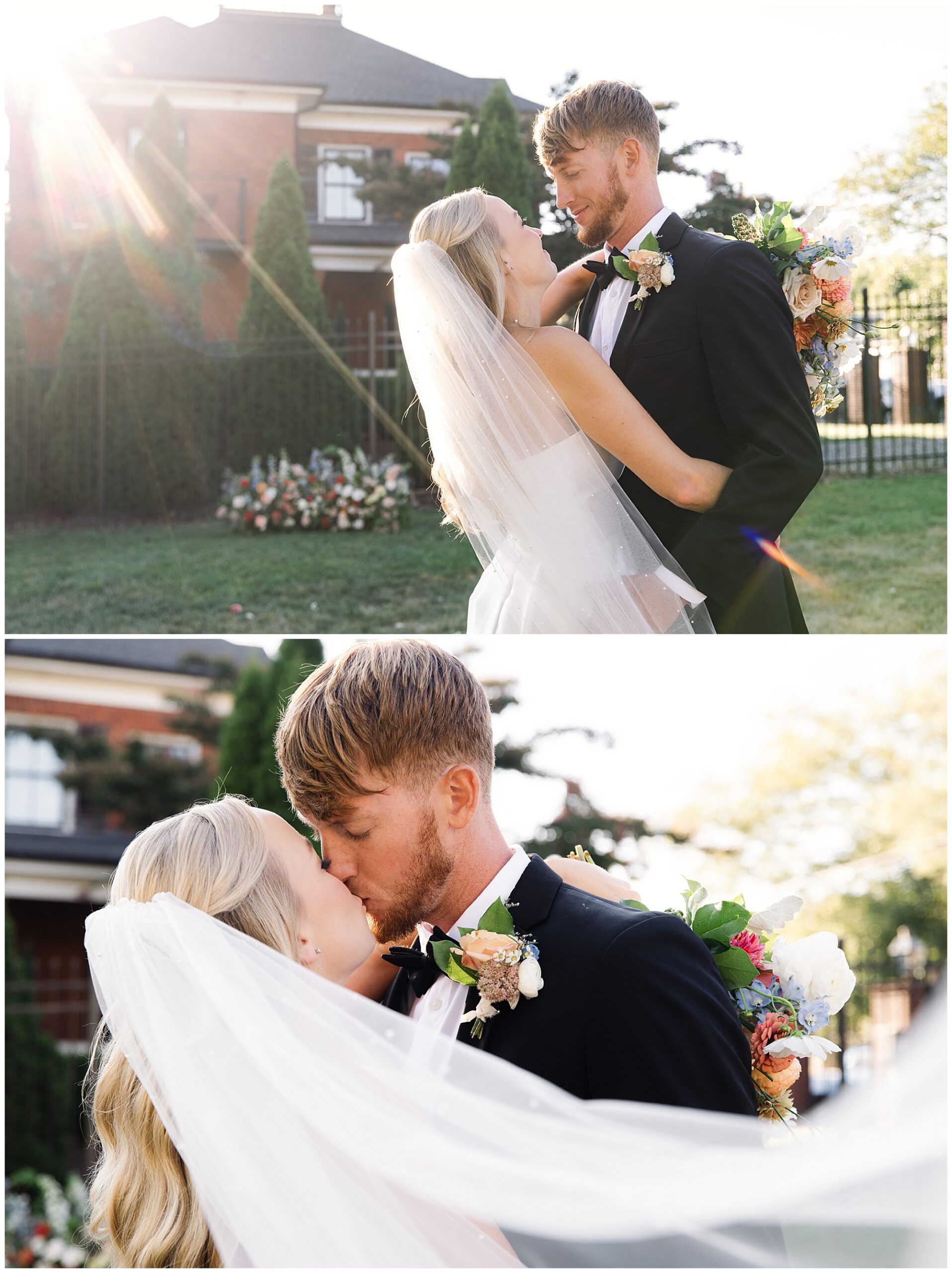 A couple dressed in wedding attire share an intimate moment and kiss outside, with greenery and a brick building in the background. The bride wears a veil and holds a bouquet.