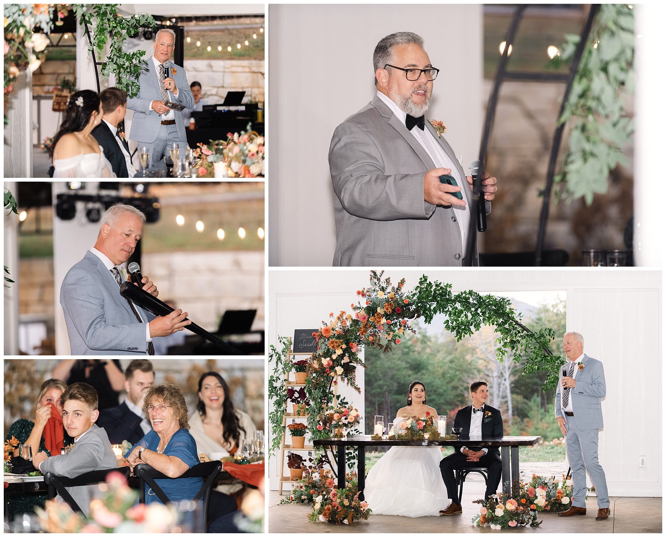 A man in a suit gives a speech at a wedding. The bride and groom sit at a table surrounded by floral decorations. Guests are seated and listening attentively.