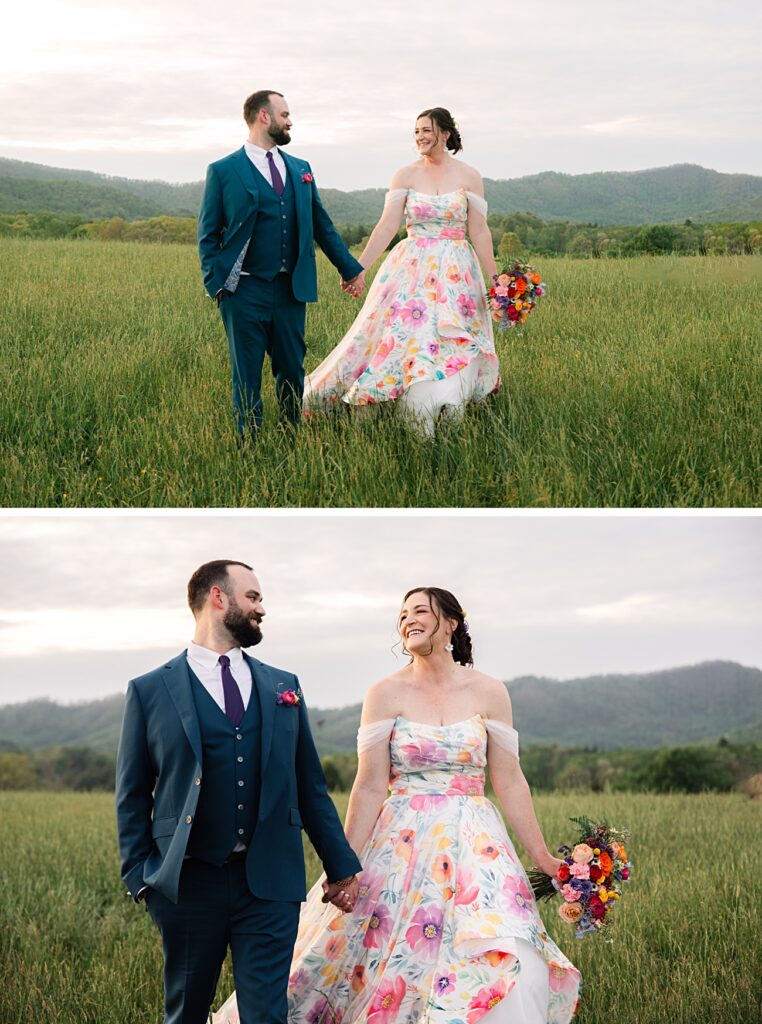 A couple in formal attire, the woman in a floral dress holding a bouquet, walk hand-in-hand through a grassy field at their Spring Garden Wedding with Asheville NC mountains in the background.