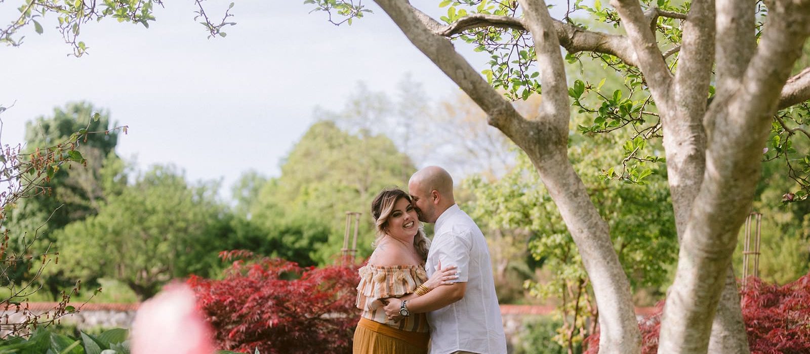 Newly engaged couple hugging one another laughing while standing outside on garden path