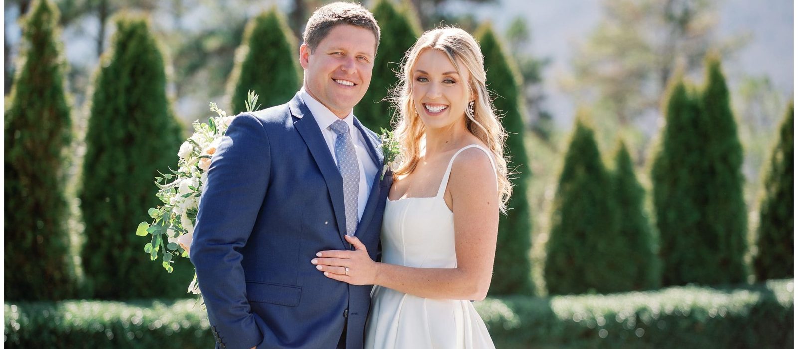 A bride and groom posing for a photo in front of bushes.